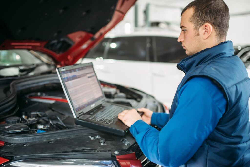 Man typing on computer under hood of vehicle services